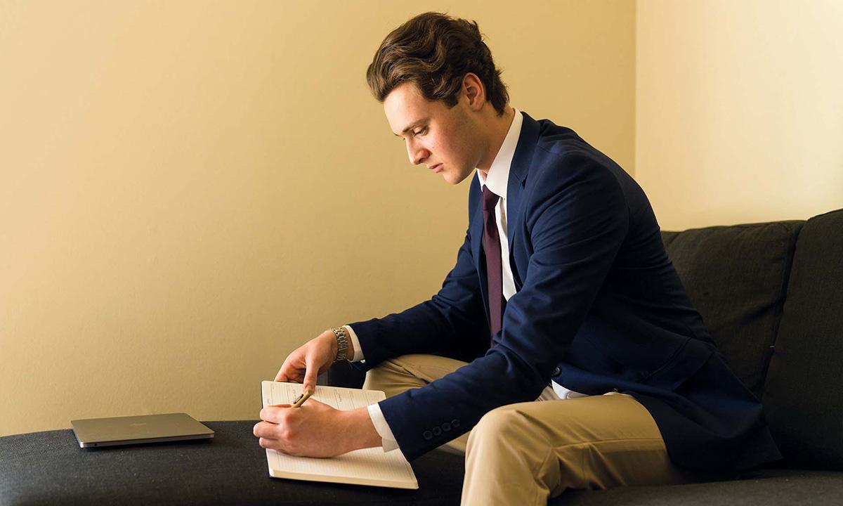 Male student sitting on chair writing in notebook